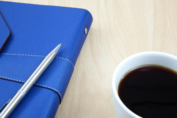 Cup of coffee on a wooden table with book and pen