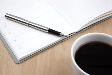 Cup of coffee on a wooden table with book and pen