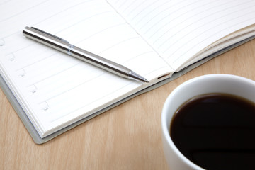 Cup of coffee on a wooden table with book and pen