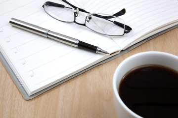 Cup of coffee on a wooden table with book and pen