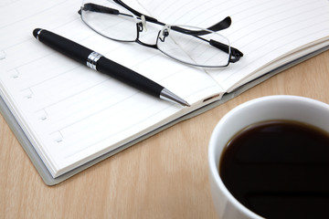 Cup of coffee on a wooden table with book and pen
