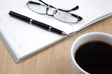 Cup of coffee on a wooden table with book and pen