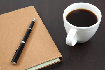Cup of coffee on a wooden table with book and pen