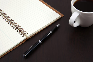 Cup of coffee on a wooden table with book and pen