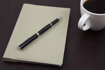 Cup of coffee on a wooden table with book and pen
