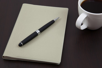 Cup of coffee on a wooden table with book and pen