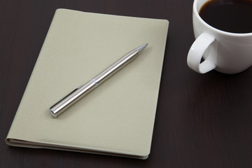 Cup of coffee on a wooden table with book and pen