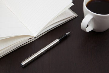 Cup of coffee on a wooden table with book and pen