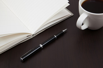 Cup of coffee on a wooden table with book and pen
