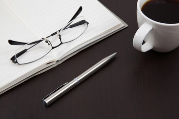 Cup of coffee on a wooden table with book and pen