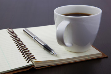 Cup of coffee on a wooden table with book and pen