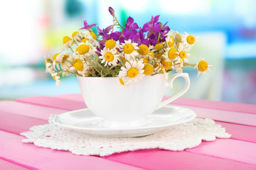 Obraz na płótnie Canvas Bouquet of chamomile flowers in cup, on bright background