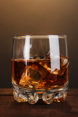 Brandy glass with ice on wooden table on brown background