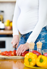 Obraz na płótnie Canvas Close up pregnant woman with knife on kitchen cuts vegetables