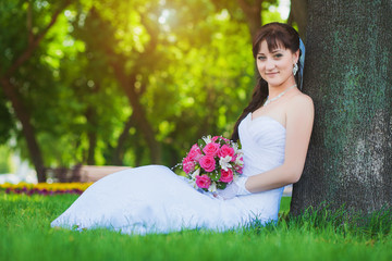 beautiful bride in white dress sitting under a tree