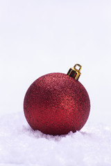 Glittery red Christmas bauble with gold topper on snow