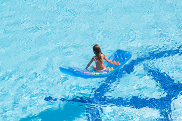 A girl sitting back on inflatable colored mattress in pool