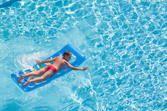 A boy floats on an inflatable mattress in pool face down