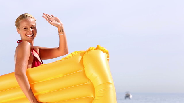 Cheerful woman waving hello and holding lilo