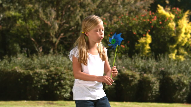 Little girl blowing a pinwheel in her garden