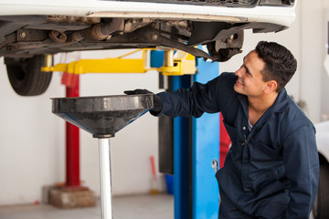 Happy young mechanic changing the oil of a car at an auto shop