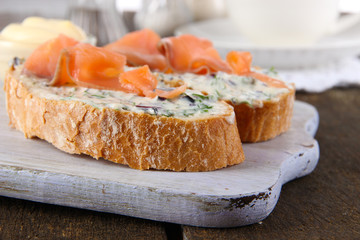 Fish sandwiches and cup of tea on cutting board on wooden table