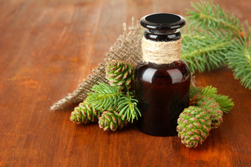 Bottle of fir tree oil and green cones on wooden background