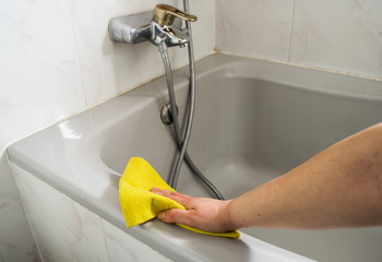 A woman cleans her Bathtub with yellow cloth
