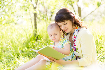 happy mother reading a book to baby in garden