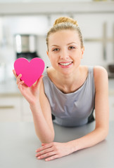 Happy young woman showing decorative heart in kitchen