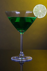 Green cocktail in martini glass on dark yellow background