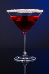 Red cocktail in martini glass on dark blue background