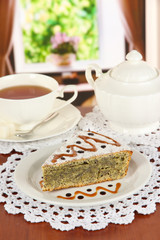 Delicious poppy seed cake with cup of tea on table in room
