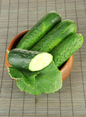 Tasty green cucumbers in wooden bowl, on bamboo mat background