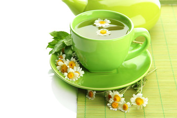 Cup and teapot of herbal tea with wild camomiles and mint,