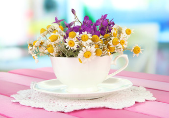 Bouquet of chamomile flowers in cup, on bright background