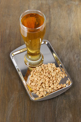 Beer in glass and nuts on tray on wooden table