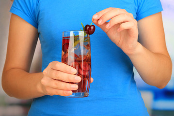 Glass of fruit drink with ice cubes in hand