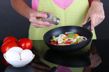 Hands cooking vegetable ragout in pan on gray background