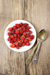 Wild strawberries on white plate, on wooden table. Copy space, s