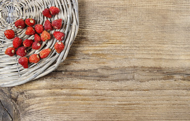 Wild strawberries on grey wicker tray, on brown wooden backgroun