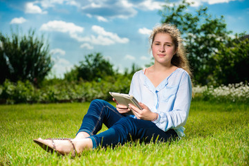 Naklejka na ściany i meble Beautiful young girl using tablet pc and sitting on the grass