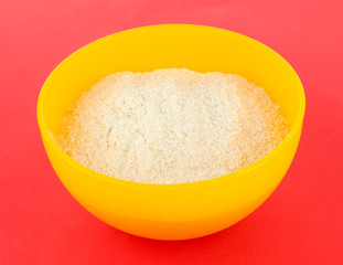 Powdered milk in bowl for baby on red background