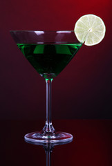 Green cocktail in martini glass on dark red background
