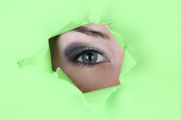 Female eye looking through hole in sheet of paper