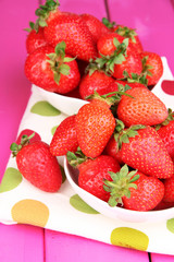 Fresh strawberry in bowl on pink wooden background