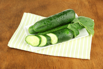 Tasty green cucumbers on color napkin, on wooden background