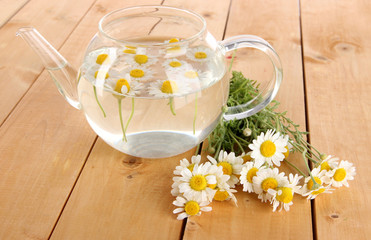 Obraz na płótnie Canvas Glass teapot with chamomile on wooden table