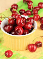 Ripe red cherry berries in bowl on wooden table close-up