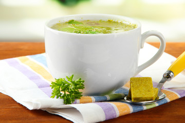 Cup of soup with bouillon cubes on wooden background